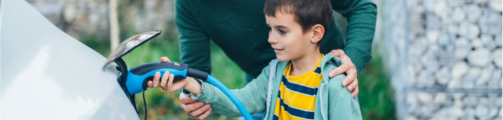 father and son charging new electric car at home banner