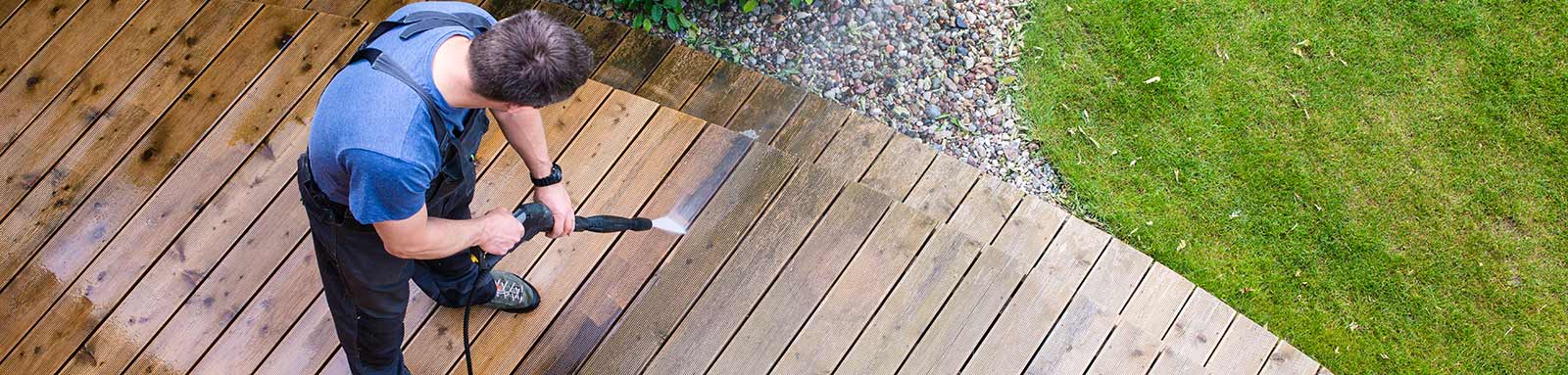 Handyman using pressure washer cleaning a wooden deck