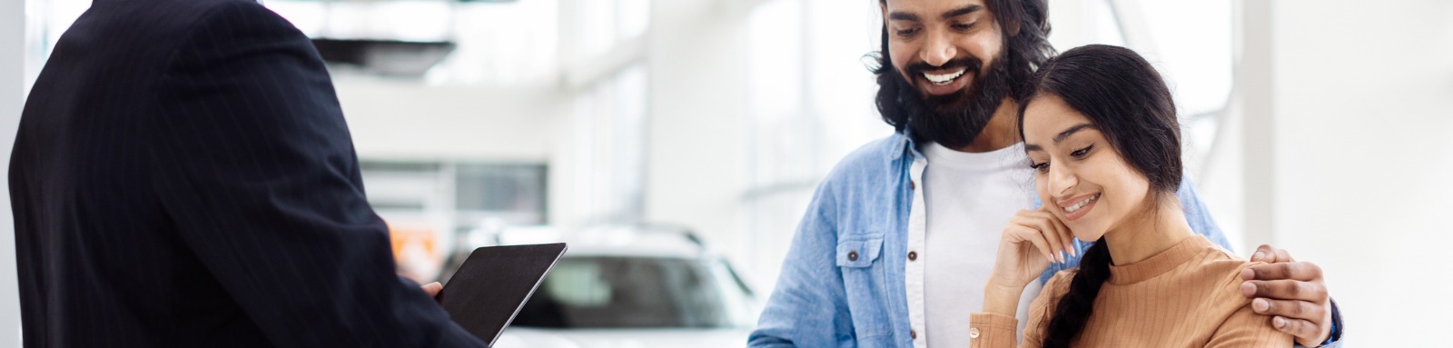 smiling couple signing documents to sell car